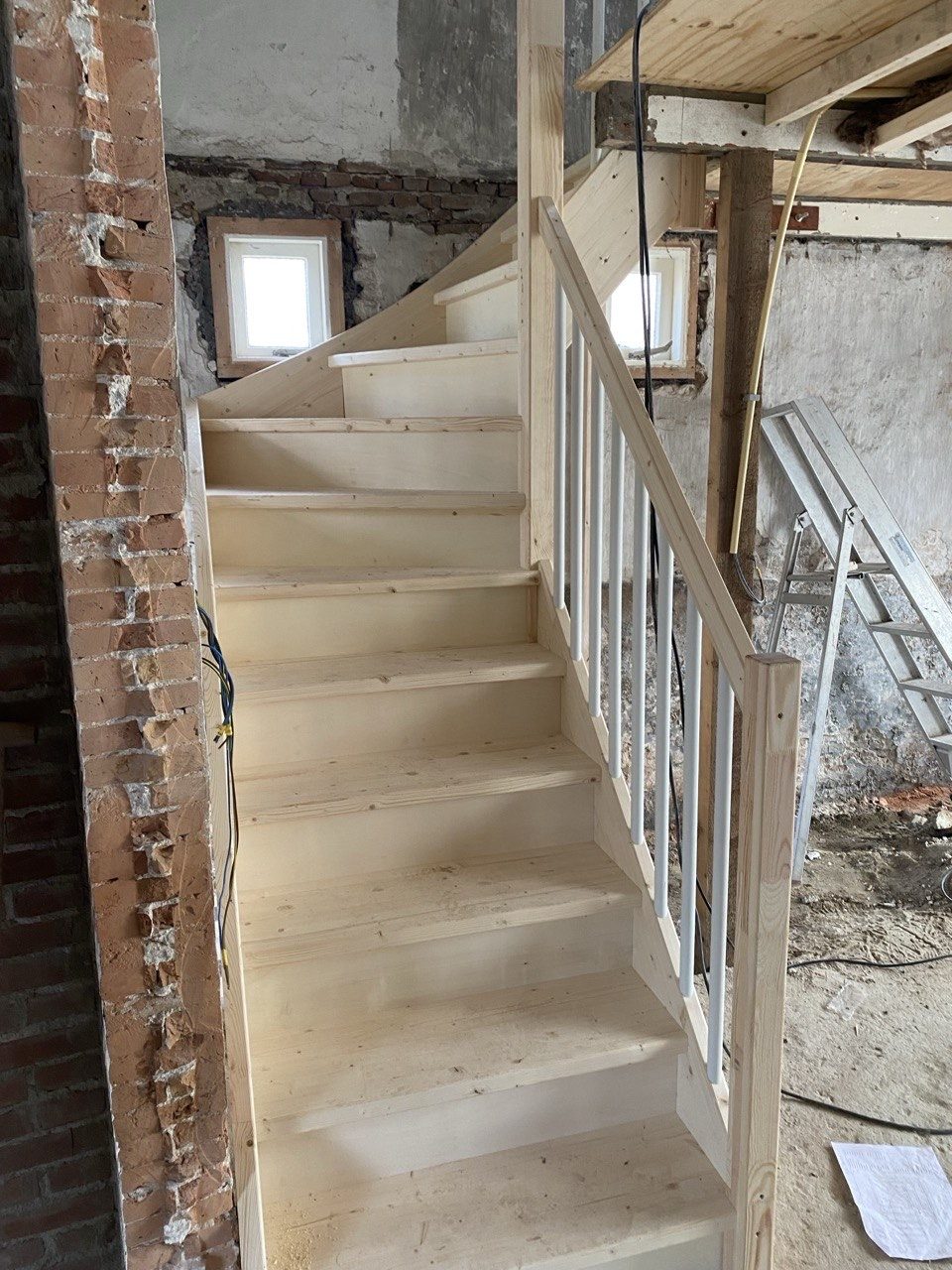 Trap met witte spijlen in een pand met zichtbaar metselwerk